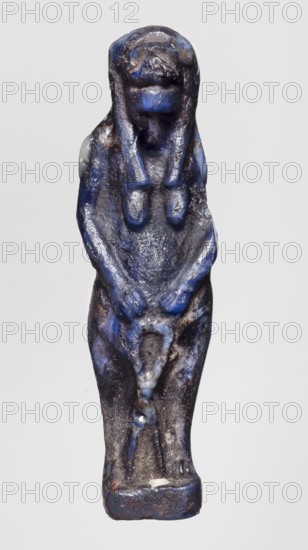 Amulet - goddess Toeris, Toeris myth., Egyptian deities, goddess, dark blue glass, 332–30 BC; Ptolemaic Period, Egypt, amulet, height 4.4 cm, width 1 cm, A small statuette depicting a standing human figure with a wig-like hairstyle and a rounded head, rendered in deep blue with patches of darker and lighter blue and areas of brownish and grayish discoloration; the figure's arms are bent and hands meet in front of the lower torso, the body shows smooth worn contours and a slightly textured surface, and the base beneath the feet is rectangular and similarly colored in blue with worn brown and gray areas.
