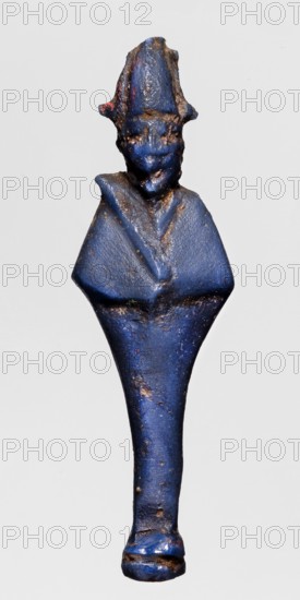 Amulet - standing god Osiris; blue glass; Osiris myth, Egyptian deities, Egyptian religion; Ptolemaic period–Roman period, 332–30 BC, Egypt; amulet; height 5 cm, width 1.4 cm., A small carved figurine rendered in a deep blue color with patches of brown and dark discoloration across its surface, showing a stylized human form with a tall pointed headdress, a simplified face with subtle features, broad shoulders forming a triangular torso, and a tapered lower body ending in a rounded base; the blue surface appears worn and slightly rough with occasional flecks of lighter and darker blue and areas of brownish corrosion or patina.
