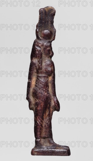 Amulet — goddess Hathor; maker, Hathor mythology, Egyptian deities, goddess; red glass; Ptolemaic Period, 332–30 BC, Egypt; amulet; height 5.2 cm, width 1.3 cm., A slender standing figurine rendered in dark brown and reddish-brown tones with areas of lighter brown and beige wear, showing a stylized human form with a taller headpiece shaped like two vertical lobes, a rounded protrusion at the face area, narrow shoulders, elongated arms hanging at the sides, and a long textured torso and legs leading to a flat rectangular base; the surface appears rough and patinated with variations in sheen and subtle highlights.