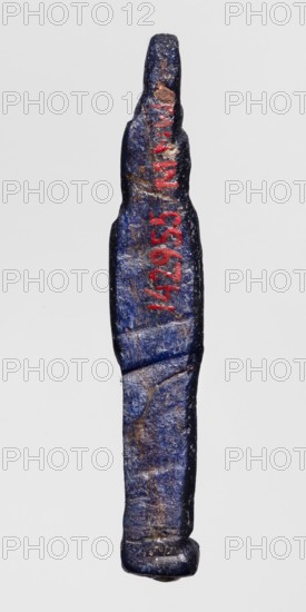 Amulet - standing goddess Isis;, Isis myth., Egyptian goddess; navy blue glass; Ptolemaic Period, 332–30 BC, Egypt; amulet; height 5.1 cm, width 3.9 cm., A narrow, elongated object with an irregular, slightly twisted shape resembling a small figurine or carved piece, shown vertically against a plain light gray background; the surface is predominantly deep blue with areas of lighter blue and worn brownish patches, and there are a few streaks of bright red visible on the upper portion; the texture appears rough and pitted with visible scratches and small dents, and the bottom end is rounded and slightly flattened while the top tapers to a narrower, uneven tip.