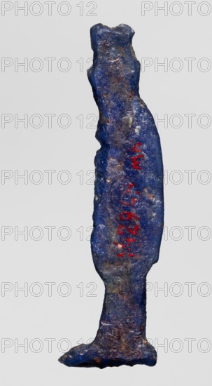 Amulet — goddess Hathor; creator, Hathor myth., Egyptian deity, goddess; dark blue glass with a touch of violet; Ptolemaic Period, 332–30 BC, Egypt; amulet; height 5.4 cm, width 1.1 cm., A narrow, elongated object shaped like a standing human figure with an irregular surface, showing a dominant deep blue color with patches of lighter blue and areas of brownish and grayish discoloration; a few small bright red marks appear along the front; the object has a slightly wider base and a tapered top with uneven edges and a rough, textured appearance.