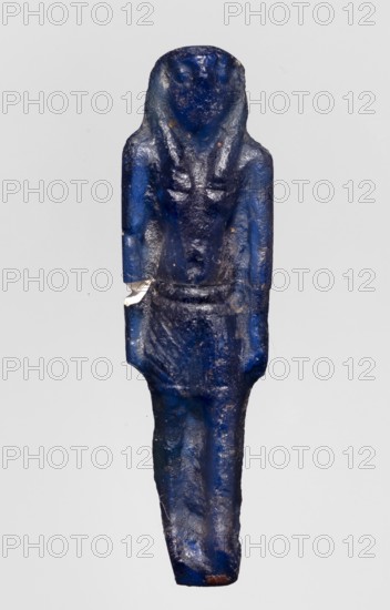 Amulet — god Horus; dark blue glass; Ptolemaic Period, 332–30 BC, Egypt; amulet; height 4.6 cm, width 1.3 cm; Horus mythology; Egyptian deities; Egyptian religion; Scen.Gal.Eg., A small blue statuette of a standing human figure with a rounded head and simplified facial features, wearing a shoulder-length headdress and a short skirt; the surface shows areas of darker and lighter blue with some small patches of brown and a few tiny shiny specks, and there is a small chipped area revealing a pale underside on one side of the torso.