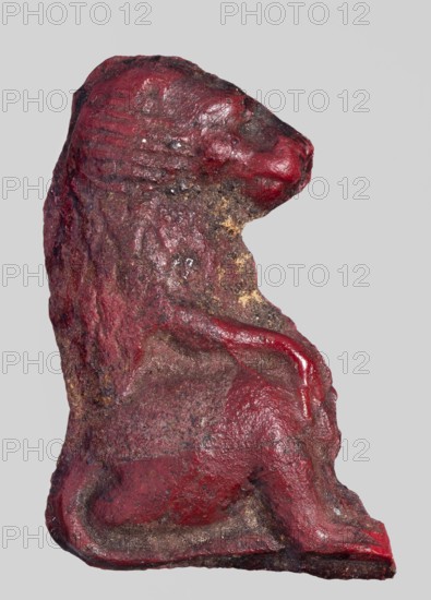 Amulet - sitting baboon; maker, baboons, sacred animals, Egyptian religion; red glass; 332–30 BC, Ptolemaic Period, Egypt; amulet; height 3.2 cm, width 2.6 cm, A sculpted object resembling an animal figure viewed in profile, with a textured, uneven surface and visible wear; the form has a rounded head, a raised snout area, a curved back, a slightly recessed midsection, a raised forelimb, and a curled tail that meets a flat base. The surface shows a mix of colors including red, dark brown, and patches of tan, with some areas appearing glossy and others matte, and small rough speckled spots scattered across the form.