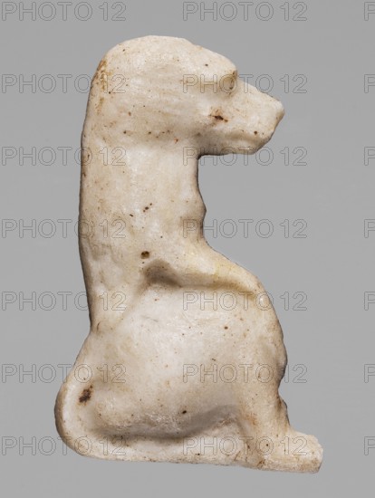 Amulet — sitting baboon; white glass; Ptolemaic Period, 332–30 BC, Egypt; height 2.2 cm, width 1.7 cm., A small sculpted figure of an animal viewed in profile, carved from a pale off-white material with a slightly rough, pitted surface and small darker speckles and spots; the figure shows a rounded head with a short snout, a curved neck leading to a compact body with a pronounced hindquarter and a tucked rear leg, and a short tail curled along the lower back; the surface displays areas of light beige and subtle brown discoloration and tiny dark flecks against the overall off-white, set against a neutral gray background.