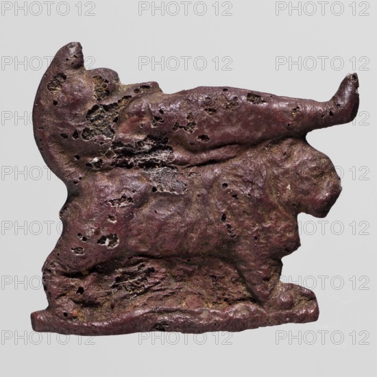 Amulet - mummy lying on a lion-shaped bed; creator, mummification bed iconography; mummies; lions; grave goods; dark red glass; 332–30 BC, Ptolemaic Period, Egypt; amulet; height 2.6 cm, width 2.9 cm, A single irregularly shaped object with a rough, pitted surface occupies the image against a plain light gray background; the object has an uneven outline with protrusions and depressions, a few small cavities and holes, and fibrous material visible in some of the cavities, showing a textured, almost layered appearance; the predominant colors visible are dark reddish-brown with areas of darker brown and touches of olive-green and muted gray, with subtle variations of lighter and darker tones across the surface.