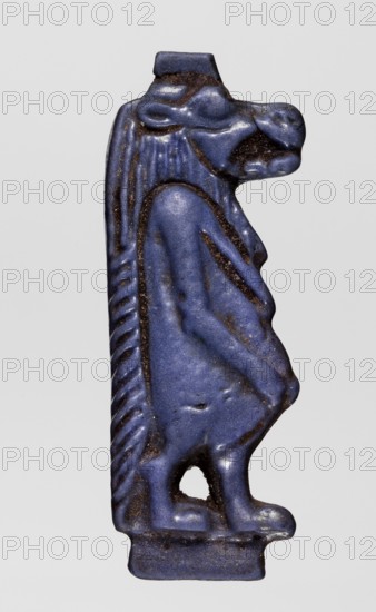 Amulet — goddess Toeris; maker, Toeris myth., Egyptian deities, Egyptian religion; navy blue glass slight violet admixture; 332–30 BC, Ptolemaic Period, Egypt; amulet; height 4 cm, width 1.4 cm, A small carved figure of a standing creature with an elongated head and snout, shown in profile, rendered in a deep blue with darker brownish-black accents along recessed lines and edges; the figure has a textured mane or hair down its back, a stylized torso and limbs with visible contours and rounded forms, a small base at the feet, and a hollowed opening near the lower body, all set against a plain light gray background.