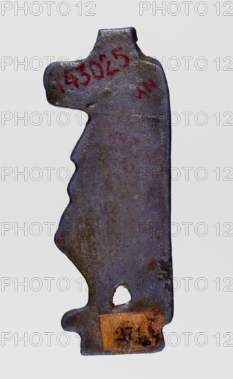Amulet - goddess Toeris; Navy blue glass slight violet admixture; 332–30 BC, Ptolemaic Period, Egypt; amulet; height 4 cm, width 1.4 cm; inscriptions/markings: Toeris myth., Egyptian deities, Egyptian religion., A roughly vertical metal object with an irregular silhouette and worn edges, showing a mottled surface in shades of blue, purple, brown, and gray, with a few small darker spots and lighter patches; there is red marking near the top and a small worn rectangular patch of brownish paper near the bottom, and a roughly oval hole above that patch.