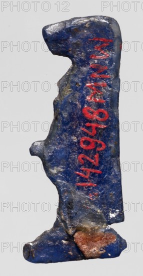 Amulet — goddess Toeris;, Dark blue glass with a violet tint; Ptolemaic Period, 332–30 BC, Egypt; amulet; height 4 cm, width 1.6 cm; depiction of Egyptian deity Toeris goddess in Egyptian religious iconography., A roughly vertical, irregularly shaped object with a textured surface in deep blue and small areas of lighter blue and gray, showing worn and rough edges and a few shiny spots; a smear of rusty brown near the lower portion and traces of darker and lighter speckling across the surface; a vertical series of bright red marks on the right side of the object; overall the object appears solid with uneven contours and a mix of matte and glossy patches.