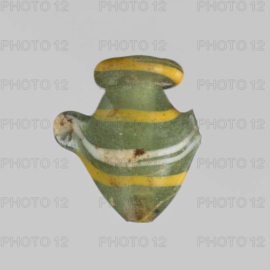 Amulet — heart ib;, found in Goluchów Greater Poland Voivodeship, Egypt; amulet representing a heart ib, used as grave equipment; New Kingdom, 18th Dynasty, ca. 1550–1295 BC; materials unspecified; height 2.2 cm, width 1.6 cm, A small glass object with a rounded top and a tapered base, showing a group of horizontal bands in green, yellow, and white; the glass surface has a matte, slightly weathered appearance with small areas of brownish discoloration and some chips along the edges, and a short protruding handle-like loop on one side.