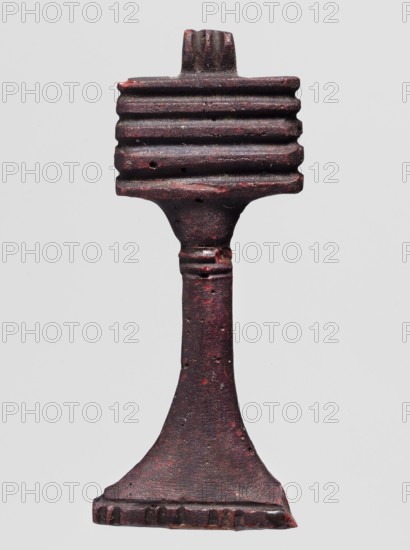 Amulet - djed pillar, A brown glass amulet in the shape of a djed pillar with five crossbars and a tall, slender leg that widens significantly at the bottom. Djed pillars iconography; protective amulet; grave goods; hieroglyphs. Ptolemaic Period, 332–30 BC, Egypt. Amulet; height 5.6 cm, width 2.1 cm., A single vertical object with a textured surface, appearing to be made of a dark reddish-brown material with areas of deeper red and small flecks of lighter color, set against a plain light gray background; the object has a rectangular top section with a series of horizontal ridges, a narrower midsection that tapers and shows a few raised rings, and a flared base that widens into a flat foot with a notched edge.