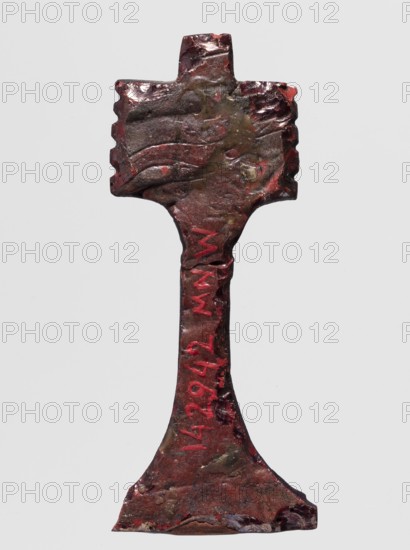 Amulet - djed pillar, A brown glass amulet in the shape of a djed pillar with five crossbars and a tall, slender leg that widens significantly at the bottom. Djed pillars iconography; protective amulet; grave goods; hieroglyphs. Amulet; 332–30 BC, Ptolemaic Period, Egypt. Height 5.6 cm; width 2.1 cm., An upright metallic object with an irregular cross-shaped top and a flared base, showing a rough, uneven surface texture with dents and ridges; the object appears primarily dark brown with areas of red and hints of greenish and ochre discoloration, and there are a few brighter red accents along the central shaft and near the edges.