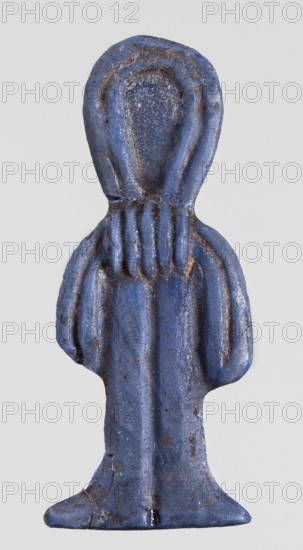 Amulet - tit;, Protective amulet in the shape of a tit knot, made of dark blue glass, with hieroglyphs. Function: grave good/amulet. Date: 332–30 BC, Ptolemaic Period, Egypt. Dimensions: height 4.6 cm, width 1.8 cm., A small sculpted figure with a rounded head and draped body, rendered in a textured blue material with areas of darker blue and small patches of brownish discoloration; the figure shows simplified folds and vertical grooves suggesting a robe and a base that flares slightly outward, with some rough surface speckling and tiny lighter spots against a plain light gray background.