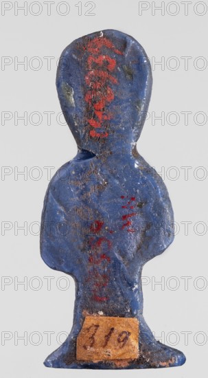 Amulet - tit, protective amulet in the shape of a tit knot made of dark blue glass, with hieroglyphs; Ptolemaic Period, 332–30 BC, Egypt; grave good; amulet, height 4.6 cm, width 1.8 cm, A small figurine-shaped object with a rounded head and broad shoulders tapering to a narrow base, painted predominantly blue with worn areas showing darker and lighter blue tones and patches of brownish wear, and with several small areas of red pigment on the head, torso, and lower body. The surface appears textured and uneven with scratches and chips, and there is a small rectangular patch of faded tan material affixed near the base. The background is a pale gray.