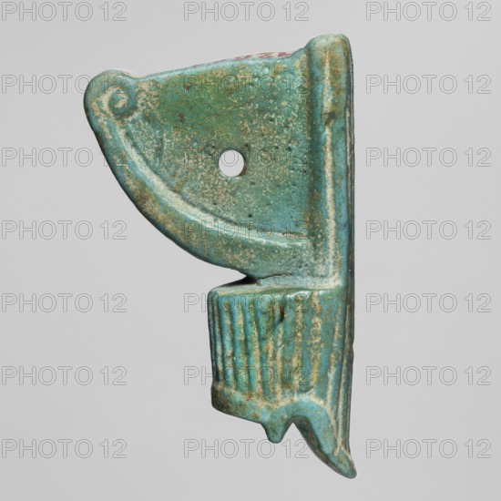 Amulet - red crown, red crown made of green-glazed faience with a hole in the field between the protruding parts of the crown; amulet of power, crowns, symbols; 664–525 BC, Late Period, 26th Dynasty, Egypt; height 4 cm, width 2.3 cm, A small object with a curved upper section and a ribbed lower section, rendered in shades of turquoise and green with areas of lighter and darker patina, showing some tan and brown speckling and wear; the curved upper part has a rounded outer edge and a circular hole near its center, while the lower ribbed section ends in a pointed projection and the piece shows textured surface variations and subtle shadowing against a plain light gray background.