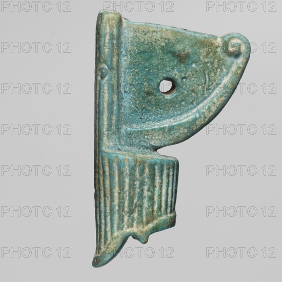 Amulet — red crown made of green-glazed faience with a hole in the field between the protruding parts of the crown; amulet of power, crown symbol; 664–525 BC, Late Period, 26th Dynasty, Egypt; height 4 cm, width 2.3 cm., A turquoise and greenish-blue carved object with a weathered, slightly rough surface, shaped with a curved upper section that has a rounded corner and a circular hole near the center, a vertical ribbed lower section with fluted grooves, and a small pointed extension at the bottom; the object shows patches of lighter and darker turquoise, areas of pale green and beige wear, and subtle brownish spots, all set against a neutral pale gray background.