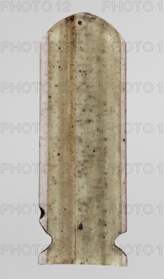 Amulet - cartouche, Goluchów Greater Poland Voivodeship, cartouches, Scen.Gal.Eg., symbols, hieroglyphs, 664–332 BC; Late Period, Egypt, amulet, height 3.1 cm, width 1 cm, A long vertical object with rounded top and shaped bottom edges, showing a central surface that is a mottled pale yellowish-beige with darker speckles and streaks, flanked by narrow pale off-white borders on both sides; the object has several small dark brown and black spots and a few rusty brown streaks, with the background a uniform light gray.