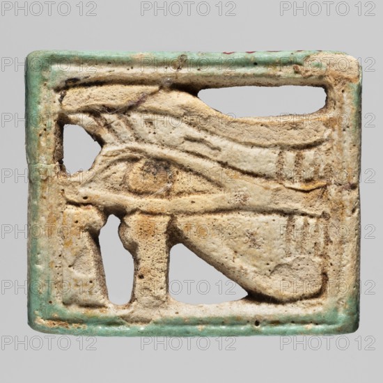 Amulet - udjat eye, udjat eye amulet, grave good associated with Egyptian religion; ca. 945–656 BC, Third Intermediate Period, 22nd–25th Dynasty, Egypt; material: amulet; height 3.2 cm, width 3.8 cm., A worn rectangular amulet with a raised carved motif showing an eye-like shape and surrounding linear details, set within a shallow frame; the surface is textured and pitted with areas of erosion and small holes, and there are visible fibers or dust caught in crevices. The color palette includes beige and off-white tones across the carved area, with spots of darker brown discoloration and flecks of yellowish staining, and a narrow greenish-blue glaze or paint along the outer edge. The background is a flat neutral gray.
