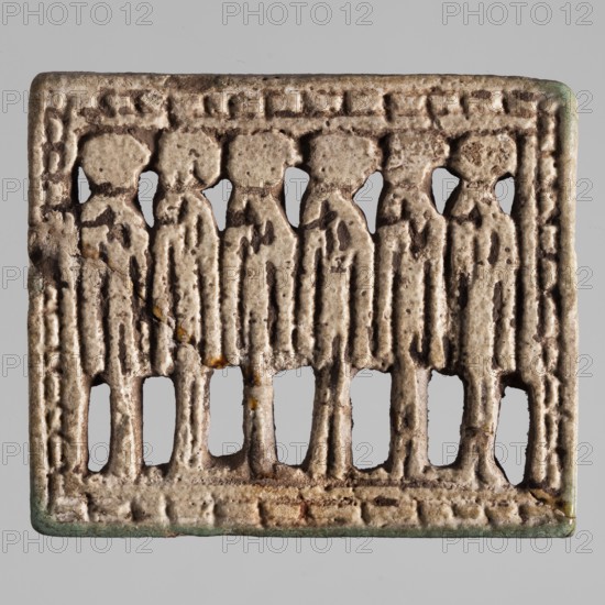 Amulet — plaque with six standing deities in a frame, Egyptian deities with solar discs; amulet made during the Late Period, 26th Dynasty, 664–525 BC, Egypt; height 4.5 cm, width 5.3 cm;, A rectangular object with a raised border and a row of several stylized standing figures in relief, each figure shown from head to lower legs with simplified rounded heads and elongated torsos; the material has a weathered, pitted surface with rough texture and small holes where the background shows through between the figures and beneath their legs; colors visible include beige, off-white, brown, darker brown accents in recessed areas, small patches of green at the corners, and tiny spots of yellowish-brown staining.