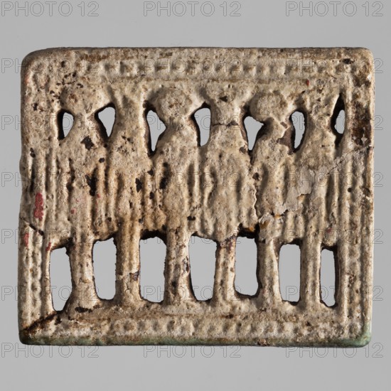 Amulet — plaque with 6 deities; maker, Egyptian deities, solar discs; Egyptian religion; 6 standing figures in a frame; 664–525 BC, Late Period, 26th Dynasty, Egypt; amulet; height 4.5 cm, width 5.3 cm., A rectangular carved object with a weathered, rough surface showing a pale beige base color with darker brown spots and patches and small areas of red and green. The top edge and bottom edge have a raised dotted border, and the central area contains a row of carved standing figures with rounded heads and draped forms, each separated by vertical ridges that continue downward into a series of rectangular cutouts along the lower half. The cutouts reveal a neutral gray background through their openings. The surface shows cracks, chips, and textured pitting, and there are darker brown stains concentrated in some recessed areas.