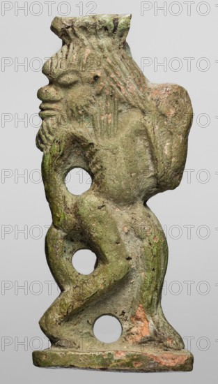 Amulet — the dancing god Bes; creator, Bes myth., Egyptian deity depicted with feathers, dancing and holding musical instruments; Egyptian religion; New Kingdom, ca. 1550–1069 BC; amulet; height 6.7 cm, width 2.8 cm., A sculpted figure viewed in profile with a textured surface showing shades of green, brown, and pinkish-orange, with a flat rectangular base and a head featuring a pronounced nose, brow, and beard; the body has a curved, sinuous form with three circular holes running vertically through it, a ridged or striated texture on the head and upper torso, and worn, rough areas and patches of discoloration throughout.