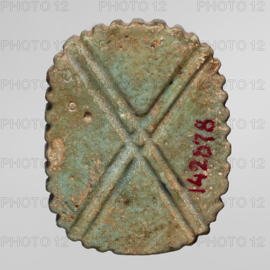Amulet — plaque with the head of the god Bes; maker, found in Goluchów Greater Poland Voivodeship; depicts Bes Egyptian deity wearing crowns; Egyptian, Late Period, 664–332 BC; amulet; height 3.4 cm, width 2.7 cm., An oval object with scalloped edges shown against a light gray background, mostly greenish-blue with areas of brownish rust and tan discoloration, featuring a raised X-shaped ridge across its surface, a few small round depressions, and a small irregular darker mark near one ridge; the colors visible include greenish-blue, brown, tan, reddish-brown, and a small area of dark bluish-black.