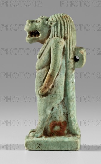 Amulet - goddess Toeris, Toeris myth., Egyptian deities, crocodiles, hippopotamuses. Figurine of the goddess Toeris in the form of a pregnant hippopotamus standing on lion legs and equipped with a crocodile tail. A stand under the legs, a pendant on the back. 664–332 BC; Late Period, Egypt. Amulet; height 5 cm, width 1.5 cm., A small statuette of a standing anthropomorphic lion figure rendered in a pale green-blue glazed material, showing a mane with vertical grooves, a snarling open mouth, and a defined nose and eyes; the figure’s arms hang down along its sides and it stands on a rectangular base. The surface shows areas of darker green and brown discoloration and a patch of reddish-brown staining near the lower front. The background is a smooth mid-gray that transitions to a lighter gray toward the bottom.