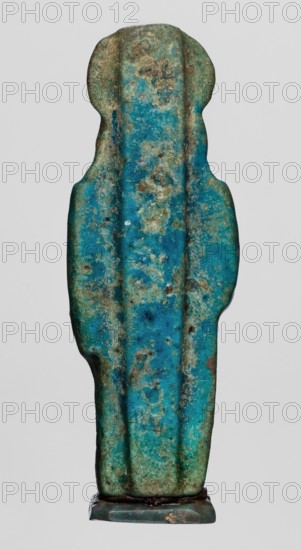 Amulet — figurine of a lion-headed goddess Sekhmet? standing with a solar disk with a uraeus on her head, holding a lotus scepter in her right hand left lowered. Possibly Wajit/Sekhmet; Egyptian deity associated with lionesses and Egyptian religion. Material: amulet; Late Period, 664–332 BC, Egypt. Dimensions: height 5.5 cm, width 1.8 cm., A vertical, elongated object with an irregular silhouette resembling a stylized figure, showing a textured surface dominated by turquoise and teal tones with patches of green and areas of brownish weathering; the object has gently rounded shoulders and a narrower lower section, with visible vertical ridges and mottled spots of darker blue and lighter pale green, and it stands on a small, flat base that shows muted dark green and brown hues.