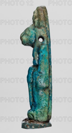 Amulet — figurine of a lion-headed goddess Sekhmet?, Sekhmet with a solar disk with a uraeus on her head, stands with a lotus scepter in her right hand left lowered. Egyptian deity; lioness. Material: amulet. Date: 664–332 BC, Late Period, Egypt. Dimensions: height 5.5 cm, width 1.8 cm., A slender vertical turquoise-green figurine with areas of darker teal and mottled brown-green patina, shown in profile against a plain gray background, with a rounded head and a pronounced snout-like projection, a smooth curving torso with subtle raised contours, a circular hole through the upper midsection, a narrow flat back edge, a textured base that is darker green with small reddish and off-white speckles, and a few spots of lighter bluish-green wear across the surface.