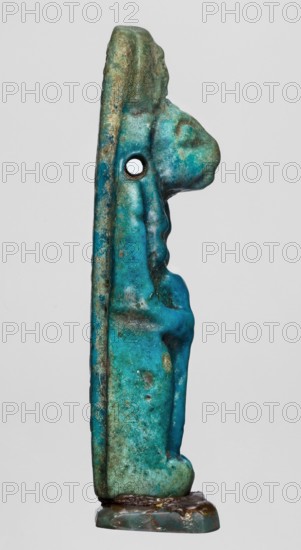 Amulet — figurine of a lion-headed goddess Sekhmet?, possibly Wajit; Egyptian deity. Sekhmet with a solar disk with a uraeus on her head, standing with a lotus scepter in her right hand left lowered. Late Period, 664–332 BC, Egypt. Amulet; height 5.5 cm, width 1.8 cm., A vertical, narrow carved object shown in profile with a patinated surface in shades of turquoise, teal, green, and hints of brown and blue, featuring a rounded protrusion near the top and an oval hole through the mid-upper area, mounted on a small rectangular base with darker brown and green tones; the surface shows uneven texture, weathered spots, and subtle raised contours suggesting carved details.