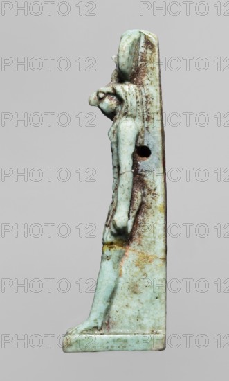 Amulet — god Re-Harakhte; maker, Re-Harakhte mythology; depicts solar disk and uraeus; Egyptian deities; Egyptian religion; Late Period, 664–332 BC, Egypt; amulet; height 4.2 cm, width 0.8 cm, depth 1.3 cm., A narrow vertical carved figure attached to a flat backing, shown in profile facing left, with a stylized head and elongated body wearing a close-fitting garment; the surface shows a weathered, pitted texture and areas of darker encrustation, and there is a round hole through the backing near the shoulder; the colors visible are pale green, light turquoise, brown, dark brown, and small areas of yellowish and reddish discoloration.