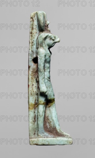 Amulet — god Re-Harakhte; maker, Re-Harakhte mythology; Egyptian deities; iconography: solar disk, uraeus; Egyptian religion; Late Period, 664–332 BC, Egypt; amulet; dimensions: height 4.2 cm, width 0.8 cm, depth 1.3 cm., A small carved figure shown in profile standing on a rectangular base against a plain gray background, the figure rendered in a greenish-blue material with areas of brown and yellow discoloration, depicting a person with an elongated head or headdress and a pronounced animal-like snout, a defined torso and arms with one arm hanging forward and the other close to the body, a short skirt with vertical texture, and legs straight down to flat feet, with surface roughness and mottled patches of darker brown and lighter greenish-blue across the object.