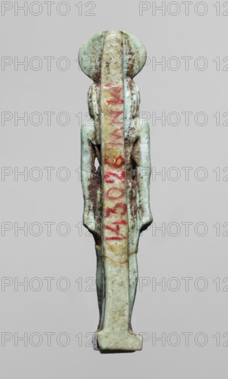 Amulet — god Re-Harakhte; maker, Re-Harakhte mythology; Egyptian deities; solar disk and uraeus iconography; Egyptian religion; dated 664–332 BC Late Period, Egypt; material: amulet; dimensions: height 4.2 cm, width 0.8 cm, depth 1.3 cm., A slender vertical object shaped like a stylized human figure viewed from the back, carved from a pale greenish-blue material with areas of brown discoloration and darker spots; the figure has a rounded head, narrow shoulders, long arms held close to the body, and straight legs ending on a rectangular base, with a central raised vertical band down the back that shows traces of a muted yellowish tone and a streak of red pigment along its length.