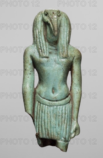 Amulet - god Thoth; maker, Goluchów Greater Poland Voivodeship; Thoth myth., Egyptian deities, Egyptian religion; 664–525 BC, Late Period, 26th Dynasty, Egypt; amulet; height 5.2 cm, width 2.1 cm, A small sculpted figure shown against a plain light gray background, rendered in a turquoise-green glazed material with areas of darker green and brownish mottling; the figure has a standing human body with broad shoulders, narrow waist, and a pleated skirt, and a head shaped like a long curved beak with stylized hair or a headdress that falls in thick locks on either side; the arms hang down alongside the torso with hands near the skirt, and the surface shows small pitted spots and subtle crackle texture in the glaze.
