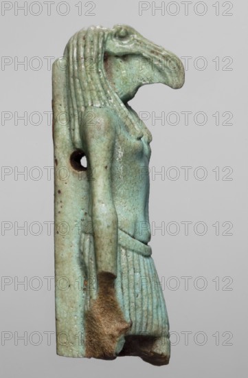Amulet — god Thoth; amulet depicting Thoth Egyptian deity; Egyptian religion; Late Period, 26th Dynasty, 664–525 BC; material not stated; height 5.2 cm, width 2.1 cm., A small carved figure shown in profile with an elongated bird-like head and beaked face, wearing a ribbed headdress and a pleated skirt; the figure is attached to a flat rectangular backpiece with a round hole near the shoulder. The surface shows a turquoise-green color with areas of pale blue and muted green, along with patches of brown discoloration and darker brown worn areas especially near the lower edge and hand. The carving displays incised lines on the headdress and skirt, a smooth torso and arm, and a slightly textured surface with small speckled spots. The background is a uniform light gray.