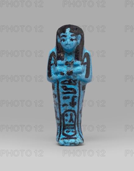Queen Henuttawi's shabti, Henuttawi queen of Egypt; ca. 1100–1000 BC. Mummy-shaped funerary figurine made of blue faience with dark-painted details. Hands crossed on the chest, right over left, holding hoes in both hands. Three-part smooth wig finished with a border; uraeus above the forehead. Round face with clearly marked eyes and eyebrows. Wide bracelets on the wrists and a necklace with a silver ornament on the chest. Facial features, wig, tools, and jewelry painted with black dye. Painted inscription in three columns on the sides and in front of the legs: Ushabti of Osiris, the king's wife, Henut-tawi, with Osiris, the great god. ca. 1069–ca. 945 BC; Third Intermediate Period, 21st Dynasty; shabti; height 12 cm, width 4.6 cm., A small figurine of a standing human form with arms crossed over the chest, rendered in bright turquoise blue with dark black painted details on the hair, facial features, shoulders, and down the front of the body; the figure has a rounded head with black-pa...