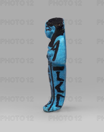 Queen Henuttawi's shabti, Henuttawi queen of Egypt; ca. 1100–1000 BC. Mummy-shaped funerary figurine made of blue faience with details in a dark color. Hands crossed on the chest, right over left, holding hoes. Wears a smooth three-part wig finished with a border; a uraeus above the forehead. Round face with clearly marked eyes and eyebrows. Wide bracelets on the wrists and a necklace with a silver ornament on the chest. Facial features, wig, tools, and jewelry painted with black dye. Painted inscription in three columns on the sides and in front of the legs reading: Ushabti of Osiris, the king's wife, Henut-tawi, with Osiris, the great god. ca. 1069–ca. 945 BC; Third Intermediate Period, 21st Dynasty, possibly from Deir el-Bahari. Shabti; height 12 cm, width 4.6 cm., A small upright figurine shown in profile with a bright blue surface and dark black painted details; the figure has a rounded head with black-painted hair, a visible face profile, and a torso with black accents suggesting...