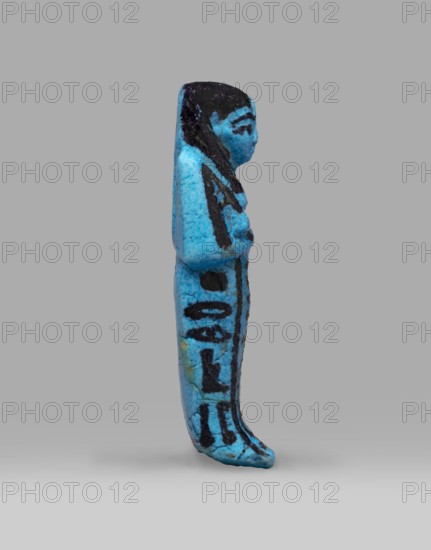Queen Henuttawi's shabti, Henuttawi queen of Egypt; ca. 1100–1000 BC. Mummy-shaped funerary figurine made of blue faience with dark-painted details. Hands crossed on the chest, right folded over left; each hand holds a hoe. Three-part smooth wig with border and uraeus above the forehead. Round face with clearly marked eyes and eyebrows. Wide bracelets on the wrists and a necklace with a silver ornament on the chest. Facial features, wig, tools and jewelry painted with black dye. Painted inscription in three columns on the sides and in front of the legs reading: Ushabti of Osiris, the king's wife, Henut-tawi, with Osiris, the great god. ca. 1069–ca. 945 BC; Third Intermediate Period, 21st Dynasty; Deir el-Bahari . Height 12 cm; width 4.6 cm., A small vertical figurine in bright turquoise blue with areas of dark black paint, shown in profile against a neutral gray background; the figure has a rounded head with black-painted hair and facial markings, a slender body with the arms held clos...