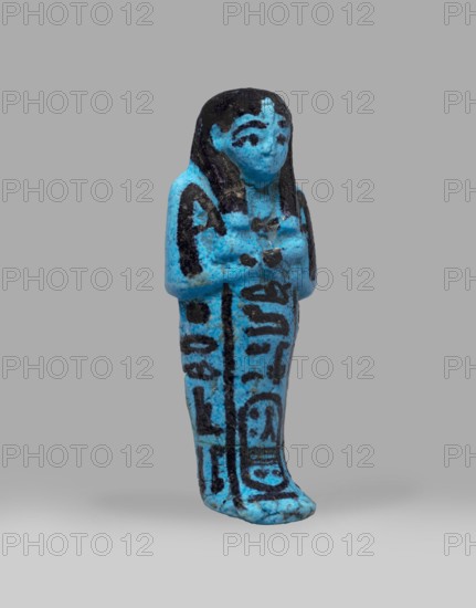 Queen Henuttawi's shabti, Henuttawi queen of Egypt; ca. 1100–1000 BC. Mummy-shaped funerary figurine made of blue faience with details in a dark color. Hands crossed on the chest, right folded over the left; both hands hold hoes. Wears a smooth three-part wig finished with a border and a uraeus above the forehead. Round face with clearly marked eyes and eyebrows. Wide bracelets on the wrists and a necklace with a silver ornament on the chest. Facial features, wig, tools, and jewelry painted with black dye. Painted inscription arranged in three columns on the sides and in front of the legs reading: Ushabti of Osiris, the king's wife, Henut-tawi, with Osiris, the great god. Attributed ca. 1069–ca. 945 BC; Third Intermediate Period, 21st Dynasty; shabti. Height 12 cm, width 4.6 cm., A small standing figurine rendered in bright blue with black painted details, showing a stylized human form with long hair, a defined face, and arms crossed over the chest; the surface has a slightly rough, ag...