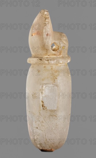 Amulet - heart with a sun disc;, sun disc iconography; protective amulet; grave goods; Late Period, Egypt, 664–332 BC; amulet; height 5 cm, width 2.5 cm, depth 1.5 cm., A translucent, elongated object with a rounded base and a carved top that resembles a stylized head or fin is centered against a plain gray background; the object shows a milky white to pale beige color with areas of cloudy translucence and faint pinkish and amber tints, and it has scattered brownish surface stains and tiny dark inclusions; a smooth collar-like ridge encircles the upper section, and a small rounded hole is visible near the carved top; the surface displays worn scratches and a few rougher patches, with a small darker brown area at the very bottom.