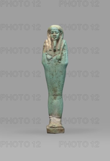 Ushabti Psamtyk-seneb, wigs, funerary figurine, hieroglyphs, beards facial hair, Psamtyk-seneb ca. 747–332 BC, back pillar, grave goods, mummy-shaped figurine standing on a base, back supported by a pillar/pilaster. Arms crossed on the chest, right folded over left. In the right hand a long-bladed hoe, in the left a pickaxe; handles of both tools rolled up at the ends. A bag on the back, slung over the left shoulder on a single string. Three-part smooth wig. Long, tapering beard braided into a plait. Engraved inscription in one column on a pilaster reading Osiris Psammetik-seneb born of Jerou justified by the voice. 664–332 BC; Late Period, Egypt. Shabti; height 12.5 cm, width 3 cm., A small figurine of a human-like figure standing upright with arms crossed over the chest, rendered in a weathered turquoise-green with areas of brownish patina and lighter beige wear, showing a stylized head with a headdress and a pronounced chin area, a tapered body narrowing toward the base, and a recta...