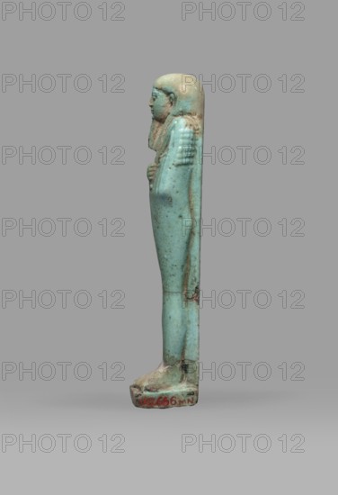 Ushabti Psamtyk-seneb, Wigs, funerary figurine, hieroglyphs, beards facial hair, Psamtyk-seneb ca. 747–332 BC. Mummy-shaped figurine, standing on a base, back supported by a pillar/pilaster. Arms crossed on the chest, right folded over left. Right hand holds a long-bladed hoe, left a pickaxe; handles of both hoes are rolled up at the ends. A bag is slung over the left shoulder on a single string. Wears a three-part smooth wig. Long tapering beard braided into a plait. Engraved inscription in one column on a pilaster: Osiris Psammetik-seneb born of Jerou justified by the voice. Date: 664–332 BC, Late Period, Egypt. Type: shabti. Height: 12.5 cm; width: 3 cm., A small upright figurine viewed in profile standing on a rectangular base, made of a smooth turquoise-blue material with areas of pale beige and brown discoloration; the figure has a rounded head with a close-fitting headdress that extends along the back, a defined facial profile, and a folded arm held against the chest; the body i...