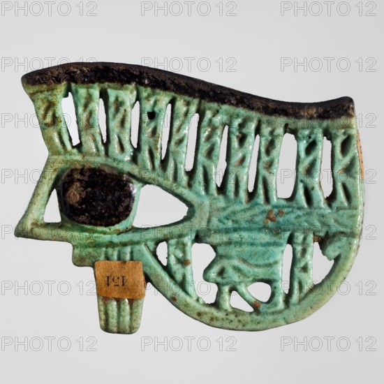 Amulet - udjat eye, udjat eyes, grave goods, Egyptian religion, baboons, 12 baboons with a small eye, ca. 945–656 BC; Third Intermediate Period, 22nd–25th Dynasty, Egypt, amulet, height 4.1 cm, width 5.2 cm, A carved, openwork object shaped like an eye with stylized surrounding elements, primarily glazed in turquoise with areas of darker green and spots of brown, and a dark brown to black glazed oval at the eye center; the piece shows textured ridges and cutouts, a darker brown rim along the top edge, and a small rectangular patch of tan attached near the lower edge.