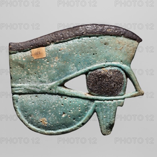 Amulet — udjat Eye of Horus; maker, provenance Goluchów Greater Poland Voivodeship; Egyptian; Third Intermediate Period, 25th Dynasty, ca. 747–656 BC; material/function: amulet associated with mummies and grave goods, Egyptian religion; dimensions: height 6.5 cm, width 7.9 cm., A turquoise and green object shaped like a stylized eye with a rounded lower portion and an extended curved upper edge, showing a textured dark brown area where the pupil would be and a few rougher dark brown spots along the top edge; the surface has a pitted, weathered texture with small irregular holes and some lighter beige encrustations, and the background is a plain light gray.