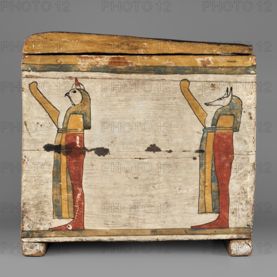 Canopic box, Goluchów Greater Poland Voivodeship; Sons of Horus, falcons, jackals, Isis, Nephthys; grave goods, Egyptian deities; ca. 747–656 BC, Third Intermediate Period, 25th Dynasty, Egypt; canopic box; height 28.5 cm, width 22 cm, depth 29 cm, The image shows a rectangular wooden box with a hinged lid, painted with a faded pale background and horizontal bands of yellow and green near the top and bottom; on the front face there is a mirrored pair of stylized standing figures facing inward, each with elongated yellow arms raised, red lower bodies, blue and yellow garments, and heads rendered in different animal-like shapes with outlines in dark paint; the surface shows areas of chipped and worn paint, small dark spots, and a few scuffs, all set against a plain gray background.