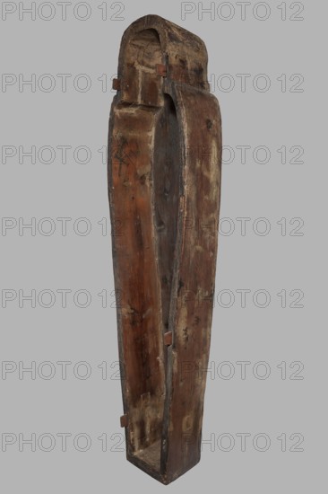 Sarcophagus of the gatekeeper of the temple of Amun Panepi, Panepy ca. 945–715 BC. Sacrificial formulas, necklace iconographic, wig iconographic, mummy straps iconographic, Nut mythological, hieroglyphs, grave goods, sculptured head. A small face with full cheeks painted red. Large eyes with black pupils and white irises. A green wig covering the ears frames the face. A loincloth above the forehead. On the chest is a large useh necklace consisting of nine stripes. On the legs is a vertical strip of the Sacrificial Formula. On the bottom of the chest is an image of Nut marked with a black outline. c. 825–715 BC; Third Intermediate Period, late 22nd Dynasty, Western Thebes. Sarcophagus; height 187 cm, width 49 cm, depth 51 cm., A tall, narrow wooden object with a curved top and an open front, showing a hollow interior and rough, worn surfaces; the wood displays a range of brown tones from dark brown to lighter, reddish-brown patches, with areas of faded beige and small dark marks; the in...