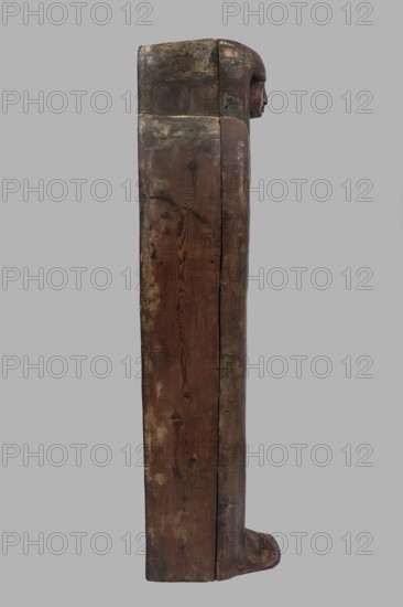 Sarcophagus of the gatekeeper of the temple of Amun Panepi, Panepy ca. 945–715 BC. Sacrificial formulas, necklace iconographic, wig iconographic, mummy straps iconographic, Nut mythological, hieroglyphs, grave goods, sculptured head. A small face with full cheeks painted red. Large eyes with black pupils and white irises. A green wig covering the ears frames the face. A loincloth above the forehead. On the chest is a large useh necklace consisting of nine stripes. On the legs is a vertical strip of the Sacrificial Formula. On the bottom of the chest is an image of Nut marked with a black outline. c. 825–715 BC; Third Intermediate Period, late 22nd Dynasty, Western Thebes. Sarcophagus; height 187 cm, width 49 cm, depth 51 cm., A tall vertical wooden object showing weathered brown and dark brown wood grain with areas of lighter beige wear, a carved human-like profile in reddish-brown at the top right, and traces of darker green and muted ochre paint near the head; the surface has a rough...