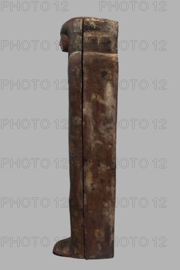 Sarcophagus of the gatekeeper of the temple of Amun Panepi, Panepy ca. 945–715 BC. Sacrificial formulas, necklace iconographic, wig iconographic, mummy straps iconographic, Nut mythological, hieroglyphs, grave goods, sculptured head. A small face with full cheeks painted red. Large eyes with black pupils and white irises. A green wig covering the ears frames the face. A loincloth above the forehead. On the chest is a large useh necklace consisting of nine stripes. On the legs is a vertical strip of the Sacrificial Formula. On the bottom of the chest is an image of Nut marked with a black outline. c. 825–715 BC; Third Intermediate Period, late 22nd Dynasty, Western Thebes. Sarcophagus; height 187 cm, width 49 cm, depth 51 cm., A tall, narrow wooden figure shown in profile with a carved human head at the top and a rectangular, elongated body extending down to a flat foot; the surface shows worn, weathered wood grain with patches of darker and lighter brown, mottled areas of beige and pal...