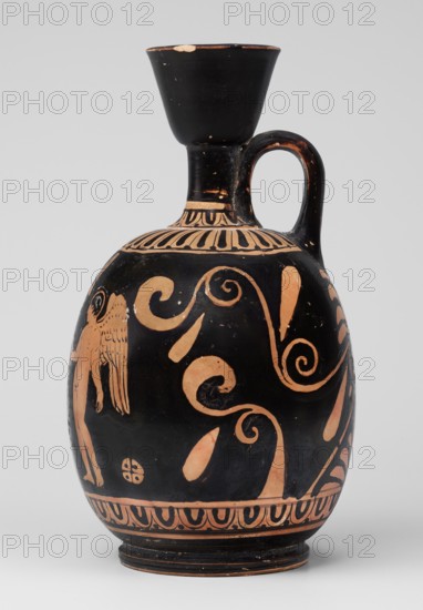 Red-figure aryballus lekythos with a scene of Aphrodite's toilet, On the belly: Aphrodite crouching and Eros handing her an alabastron, beginning of the 4th century BC previously dated to the 2nd quarter of the 4th century BC, findspot Nola, origin Campania, vessel: lekythos aryballus lekythos, height 16.5 cm, width 19.5 cm, weight 0.23 kg, subjects: Aphrodite, Eros, Greek deities., A black ceramic vessel with a rounded body, narrow neck, flared rim, and a single handle, decorated with orange-colored painted figures and swirling motifs; the upper neck area shows a band of vertical petal-like shapes in orange, the body features large scrolling tendrils and teardrop forms in orange against the black background, and a partial human-like figure with wings rendered in orange is visible on one side; the base has a repeating orange decorative border and the rim and handle show small areas where the black surface is chipped, revealing an orange underlayer.