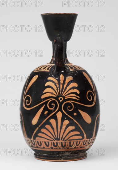 Red-figure aryballus lekythos with a scene of Aphrodite's toilet, On the belly: Aphrodite crouching and Eros handing her an alabastron, beginning of the 4th century BC previously dated to the 2nd quarter of the 4th century BC, findspot Nola, origin Campania, subject: Eros and Aphrodite Greek deities, vessel type: lekythos aryballus lekythos, height 16.5 cm, width 19.5 cm, weight 0.23 kg, A ceramic vessel with a rounded body, narrow neck, and flaring rim, featuring a single handle connecting neck and shoulder; the surface shows a polished black background with terracotta-colored decorative motifs including stylized palmettes, curving spirals, teardrop shapes, and a band of repeating petal-like forms near the base; the rim interior appears black, and there are small areas of wear where the terracotta color shows through.