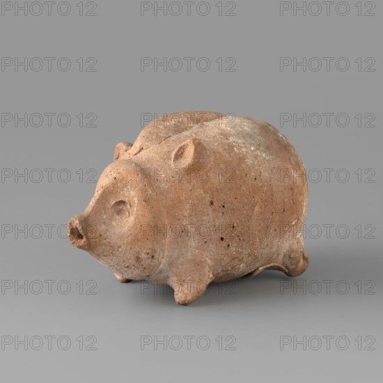 Pig-shaped rattle. A small ceramic figurine in the shape of a pig, likely a toy rattle. The animal stands on small legs; the oval muzzle is schematic and the eyes are asymmetrical, with a hole at the nose. Ears are triangular and placed at different heights, matching the limbs in shape and size. The pig has a clearly defined tuft of hair. On the right front leg there is a preserved white pelmet no. 403. 6th–3rd century BC earlier dating: 6th–5th century BC. Possibly Greece or Cyprus. Toy, ceramics. Height 5.4 cm, width 4.5 cm, depth 7.5 cm, weight 0.05 kg., A small rounded sculpture resembling an animal with a snout and small ears sits on a flat surface; the object appears textured and pitted with a weathered, earthy surface showing shades of brown and tan, with lighter beige spots and subtle darker speckles, while the background and surface beneath are smooth and medium gray.